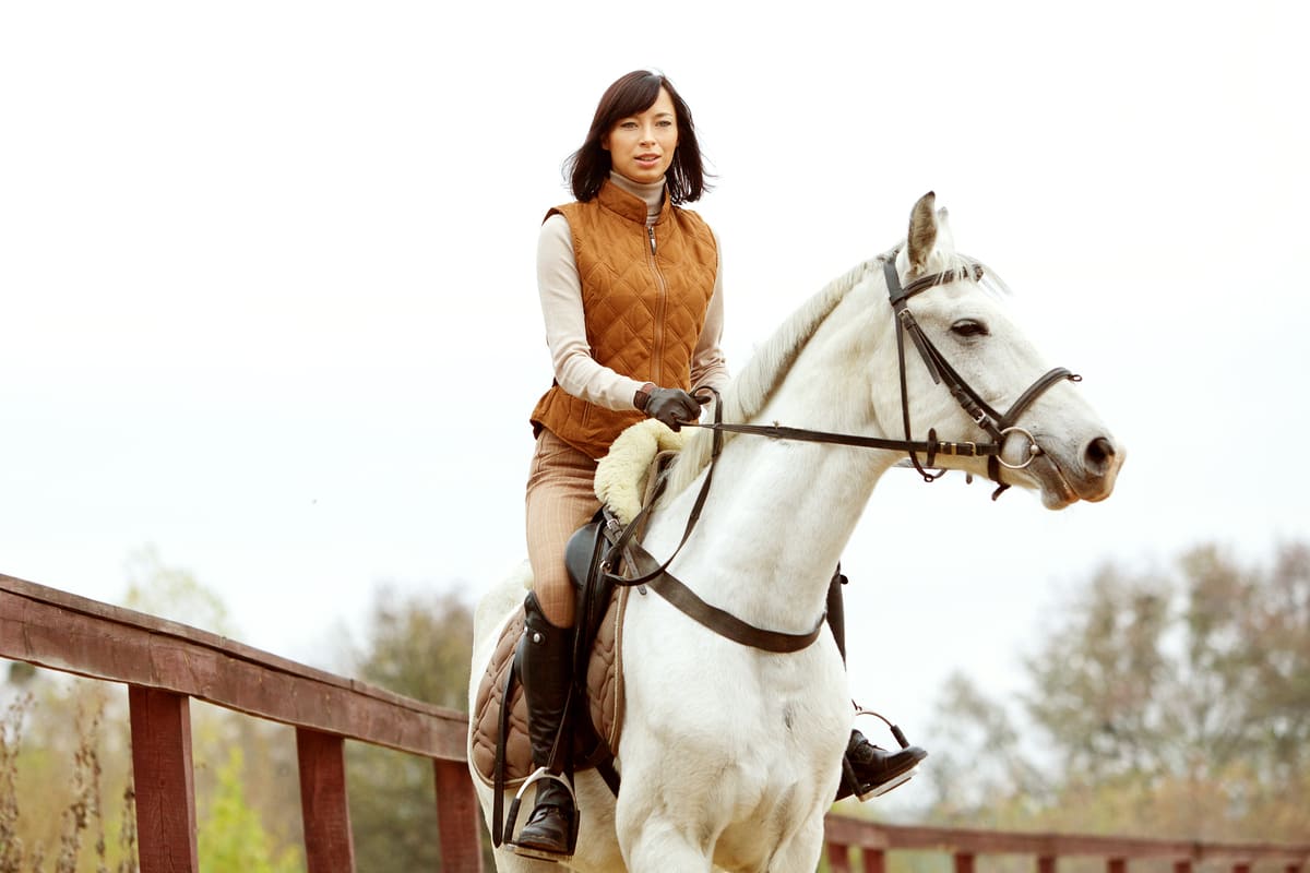 Woman riding a white horse wearing winter gear